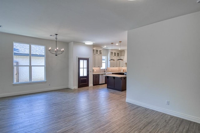 unfurnished living room with a notable chandelier, a healthy amount of sunlight, dark wood-style flooring, and baseboards