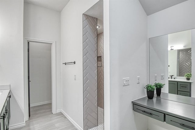 bathroom featuring vanity, wood finished floors, baseboards, and a tile shower