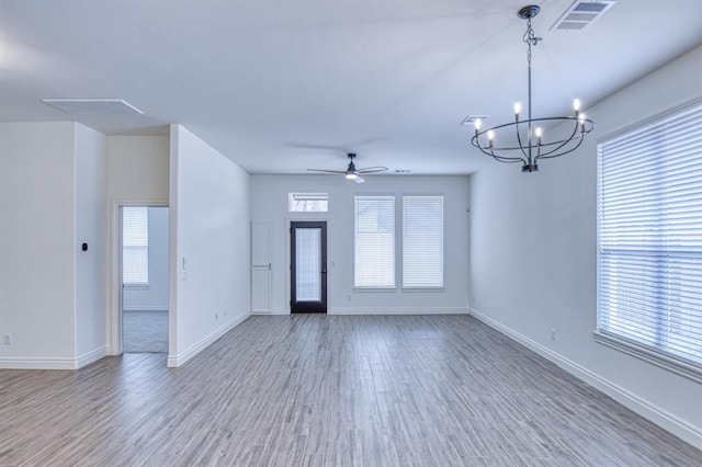 unfurnished living room with ceiling fan with notable chandelier, wood finished floors, visible vents, and baseboards