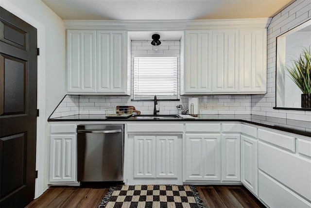 kitchen with stainless steel dishwasher, dark countertops, a sink, and white cabinetry