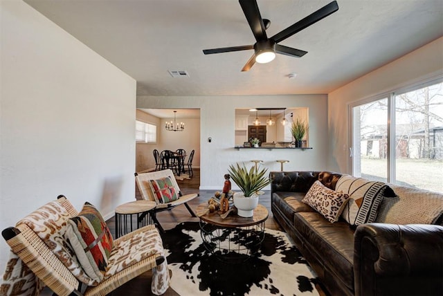 living area with wood finished floors, visible vents, baseboards, and ceiling fan with notable chandelier