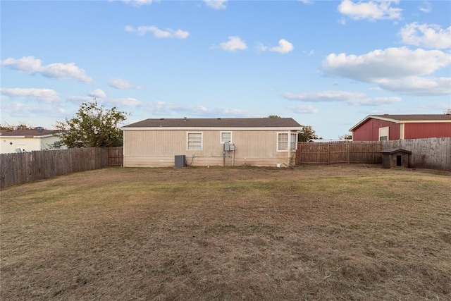 rear view of house with central air condition unit, a fenced backyard, and a yard