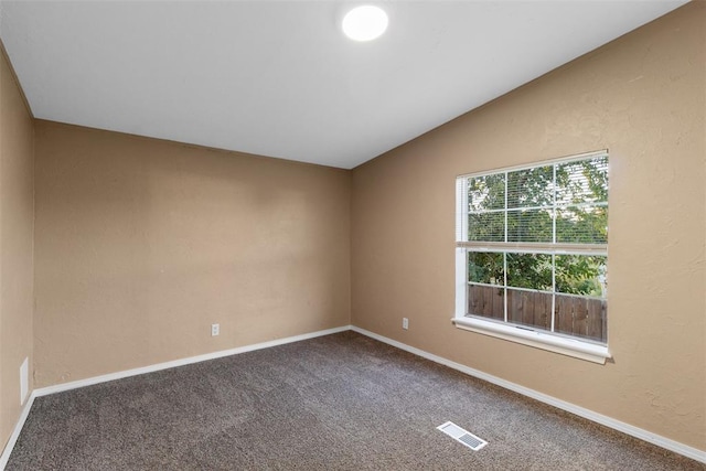 carpeted empty room with visible vents, vaulted ceiling, and baseboards