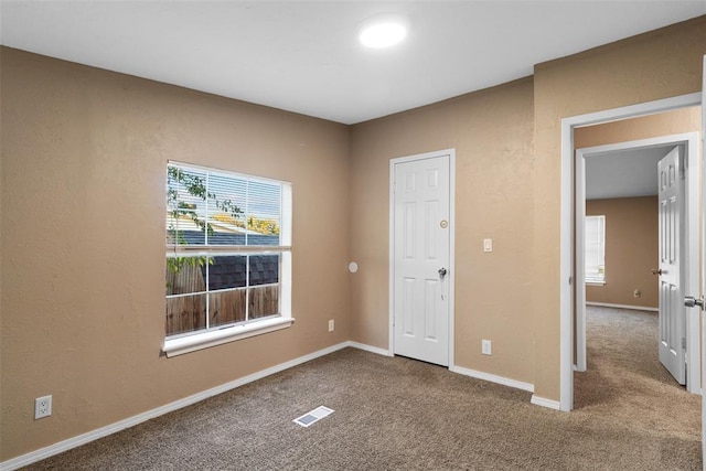 carpeted spare room featuring visible vents, a textured wall, and baseboards