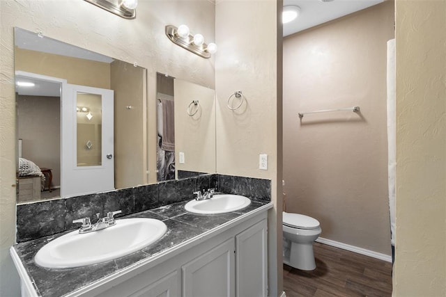 bathroom featuring double vanity, a sink, toilet, and wood finished floors