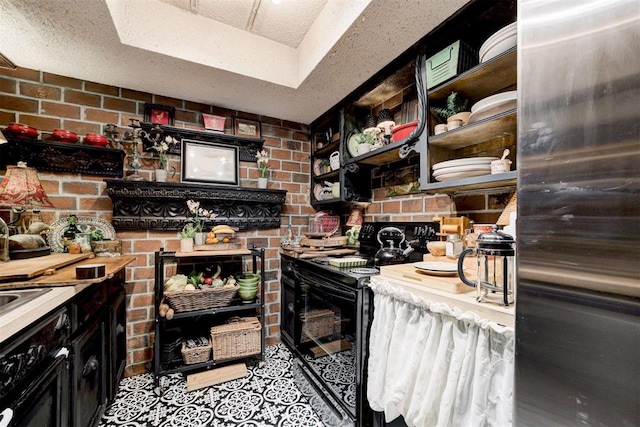 kitchen with a textured ceiling, light countertops, black range with electric cooktop, and brick wall