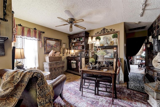 interior space featuring a ceiling fan, visible vents, a textured ceiling, and wood finished floors