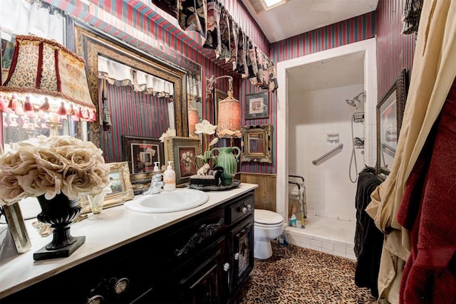 bathroom with toilet, vanity, wainscoting, a stall shower, and wallpapered walls