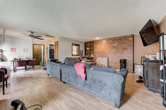 living area with a brick fireplace, visible vents, light wood-style flooring, and a textured ceiling