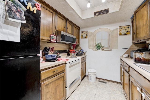 kitchen featuring brown cabinetry, stainless steel microwave, freestanding refrigerator, light countertops, and white electric range