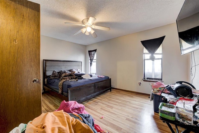 bedroom featuring light wood-style flooring, baseboards, ceiling fan, and a textured ceiling