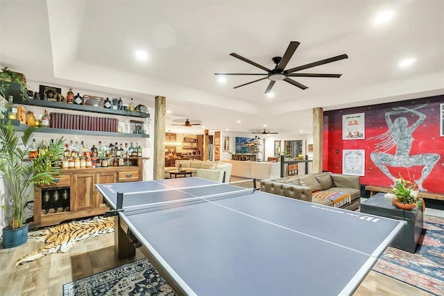 rec room featuring ceiling fan, a raised ceiling, wood-type flooring, and bar area