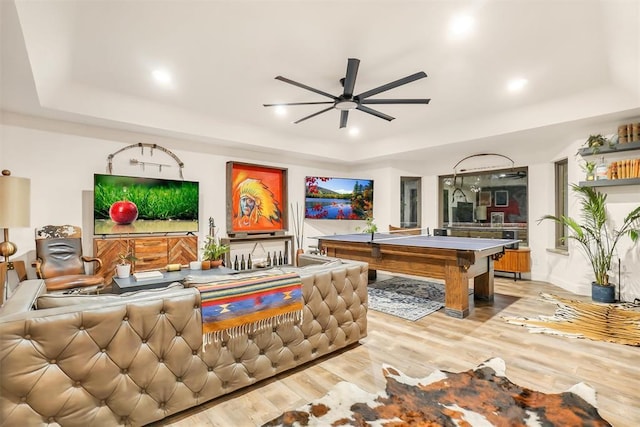 game room with light hardwood / wood-style flooring, ceiling fan, and a raised ceiling