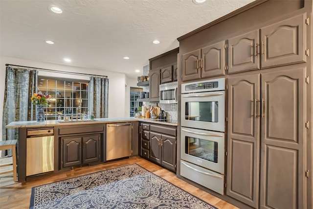 kitchen with tasteful backsplash, stainless steel appliances, light hardwood / wood-style floors, sink, and kitchen peninsula