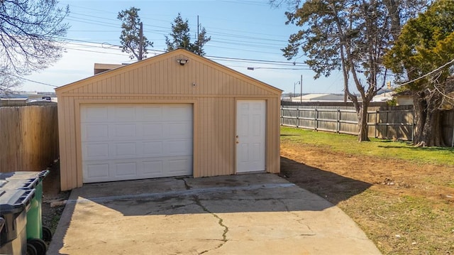 detached garage featuring concrete driveway and fence