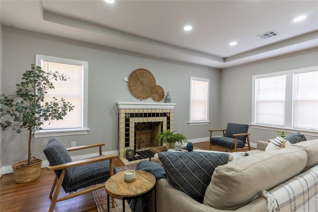 living room featuring baseboards, visible vents, a raised ceiling, a tile fireplace, and wood finished floors