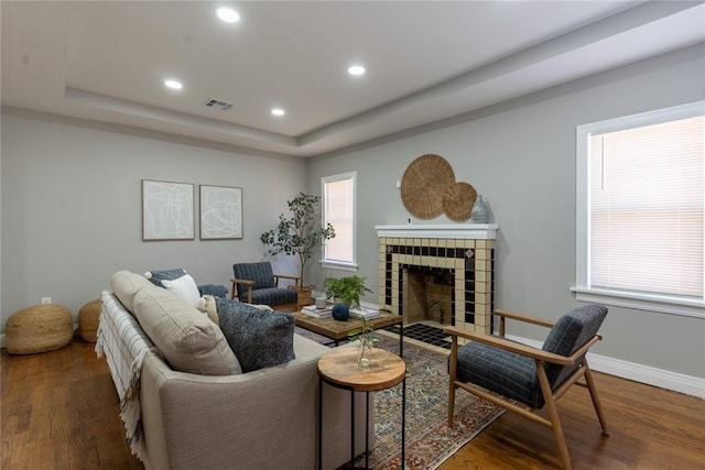 living area featuring wood finished floors, a tiled fireplace, a raised ceiling, and visible vents