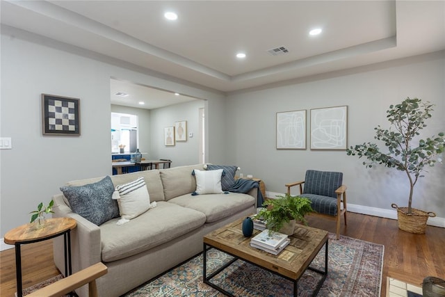 living room featuring a tray ceiling, recessed lighting, visible vents, wood finished floors, and baseboards