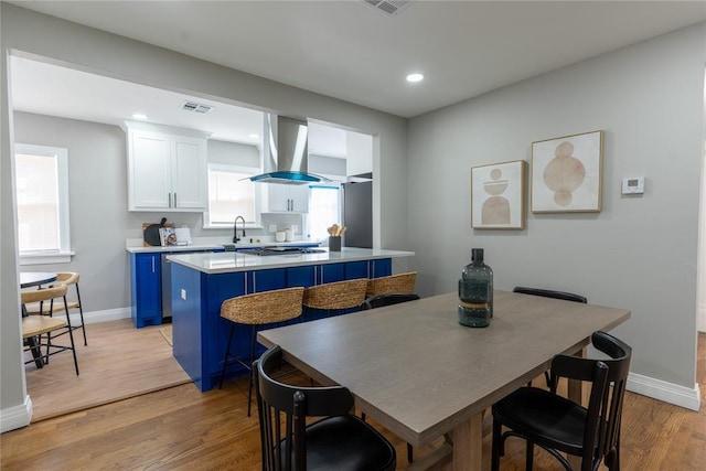 kitchen with light wood finished floors, visible vents, white cabinetry, blue cabinets, and exhaust hood