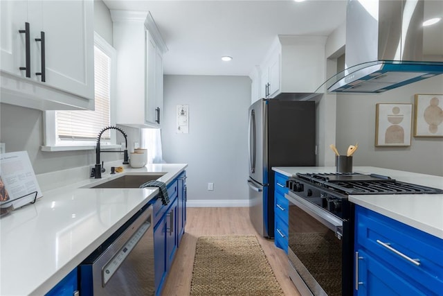 kitchen with stainless steel appliances, white cabinetry, a sink, wall chimney range hood, and blue cabinets