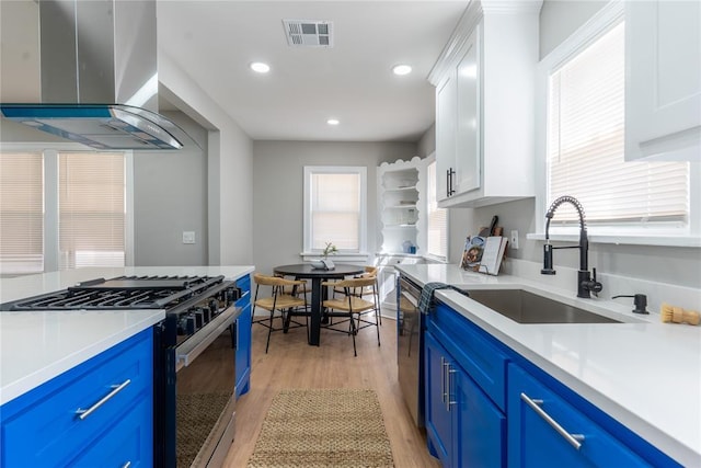 kitchen with visible vents, wall chimney exhaust hood, gas range, and blue cabinets