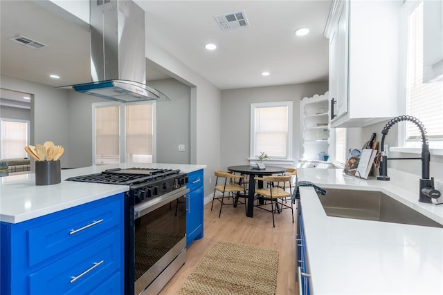 kitchen with blue cabinets, range hood, visible vents, and gas range