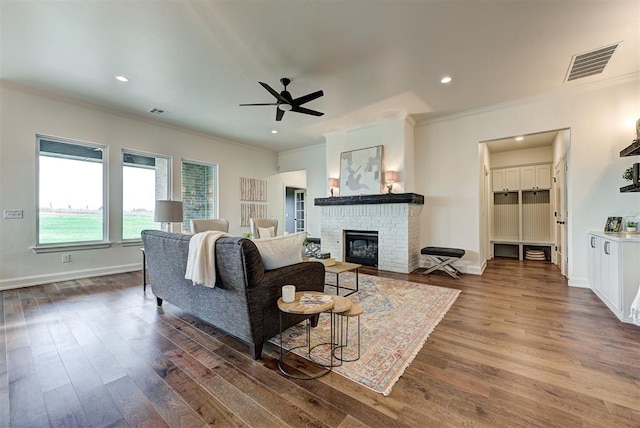 living room featuring a fireplace, ornamental molding, dark wood-type flooring, and ceiling fan