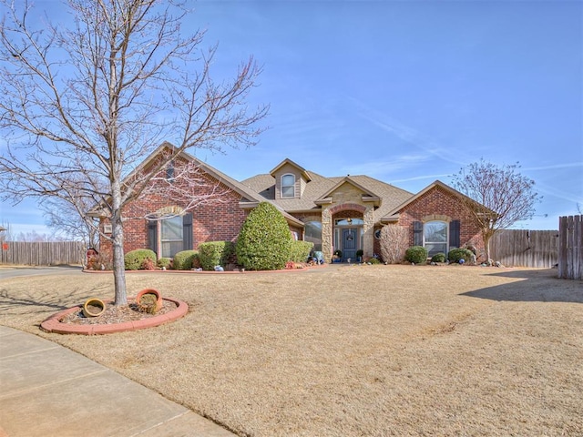 view of front of home featuring fence, brick siding, and a front lawn