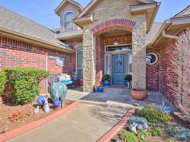 doorway to property with brick siding, roof with shingles, and stone siding