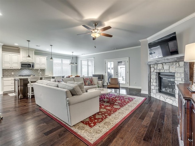 living room with ceiling fan, ornamental molding, dark hardwood / wood-style floors, and a stone fireplace