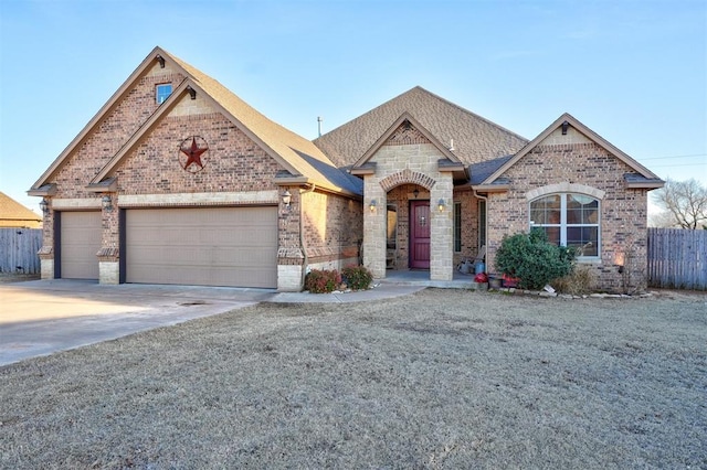 french country style house with a garage, brick siding, fence, concrete driveway, and roof with shingles