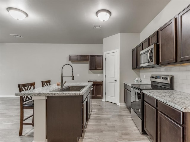 kitchen with a center island with sink, appliances with stainless steel finishes, sink, a kitchen breakfast bar, and tasteful backsplash