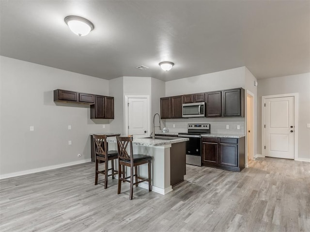 kitchen with appliances with stainless steel finishes, a center island with sink, a breakfast bar area, dark brown cabinetry, and sink