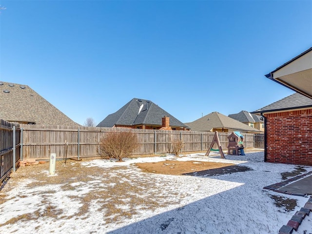 snowy yard with a playground and a fenced backyard