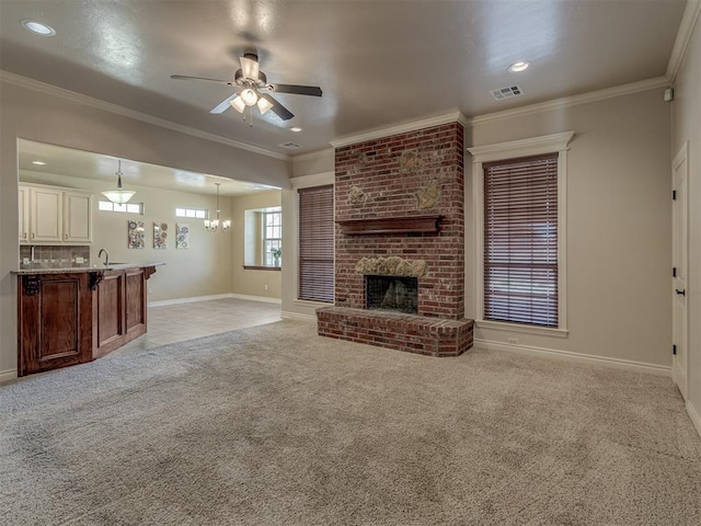 unfurnished living room with light carpet, ceiling fan with notable chandelier, a fireplace, visible vents, and ornamental molding