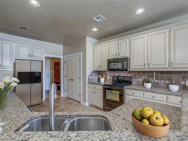 kitchen featuring a sink, light stone countertops, black appliances, white cabinetry, and backsplash