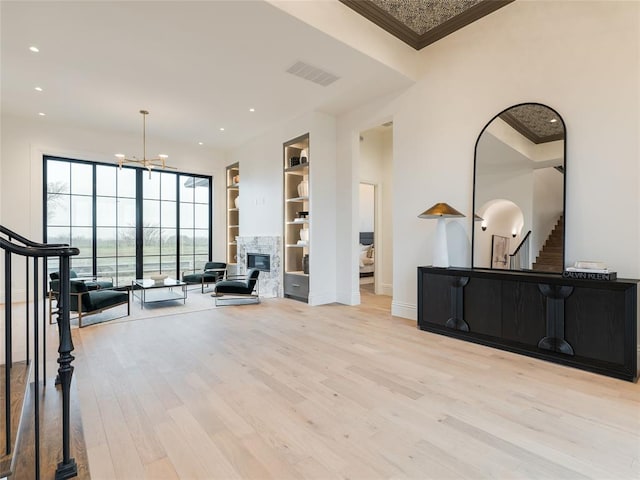 living area featuring built in shelves, a chandelier, a fireplace, ornamental molding, and light wood-type flooring