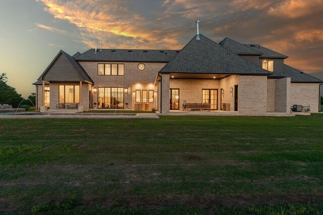 20945 Alba Ct, Edmond, OK 73012 - back of house at dusk with a patio, a lawn, brick siding, and roof with shingles