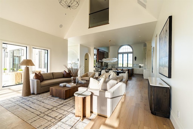20945 Alba Ct, Edmond, OK 73012 - living area featuring light wood-style flooring, high vaulted ceiling, arched walkways, a chandelier, and baseboards