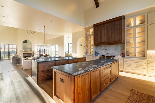 20945 Alba Ct, Edmond, OK 73012 - kitchen featuring high vaulted ceiling, a center island with sink, light wood-style flooring, arched walkways, and a fireplace