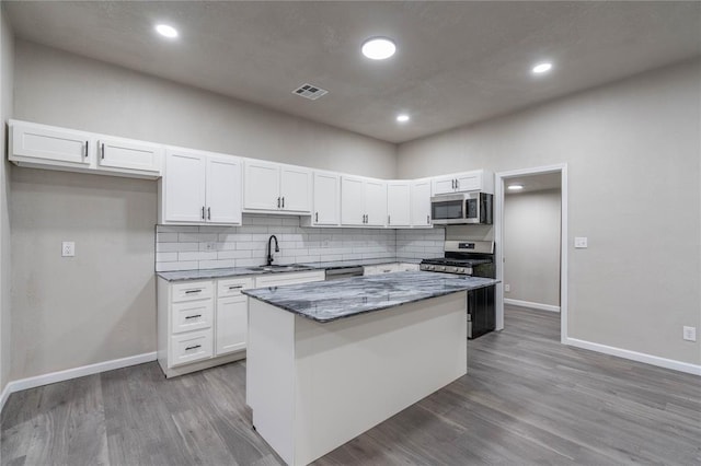 kitchen with white cabinetry, stainless steel appliances, a kitchen island, sink, and dark stone counters