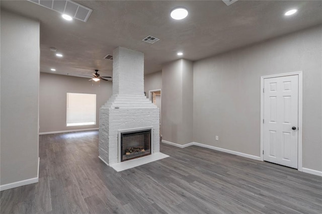 unfurnished living room featuring dark hardwood / wood-style flooring, ceiling fan, and a large fireplace