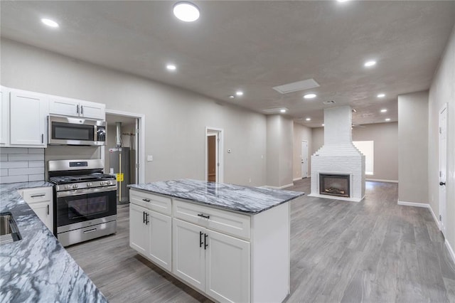 kitchen featuring white cabinets, appliances with stainless steel finishes, light stone counters, and light hardwood / wood-style flooring