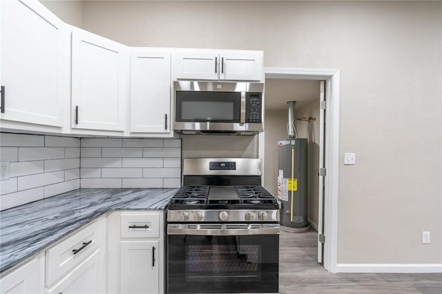 kitchen featuring stainless steel appliances, white cabinetry, light stone counters, and water heater