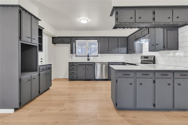 kitchen featuring light wood-style floors, appliances with stainless steel finishes, a peninsula, gray cabinets, and under cabinet range hood