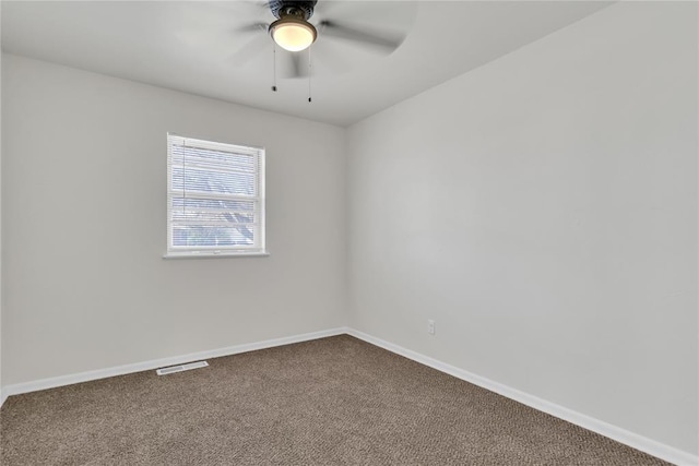 spare room featuring dark colored carpet, visible vents, ceiling fan, and baseboards