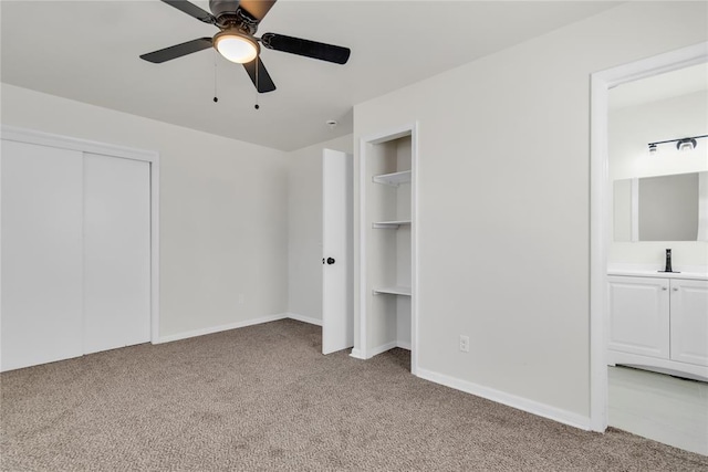 unfurnished bedroom with light carpet, baseboards, a ceiling fan, ensuite bath, and multiple closets