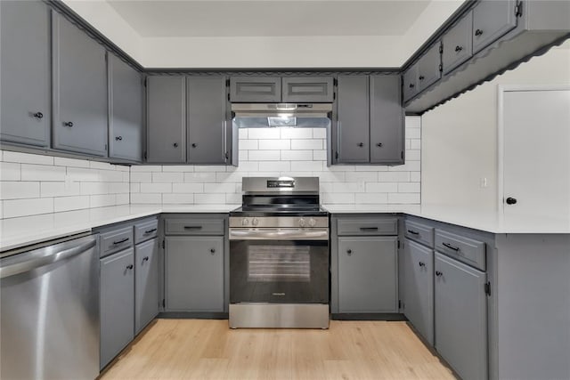 kitchen with tasteful backsplash, gray cabinets, appliances with stainless steel finishes, light wood-type flooring, and under cabinet range hood