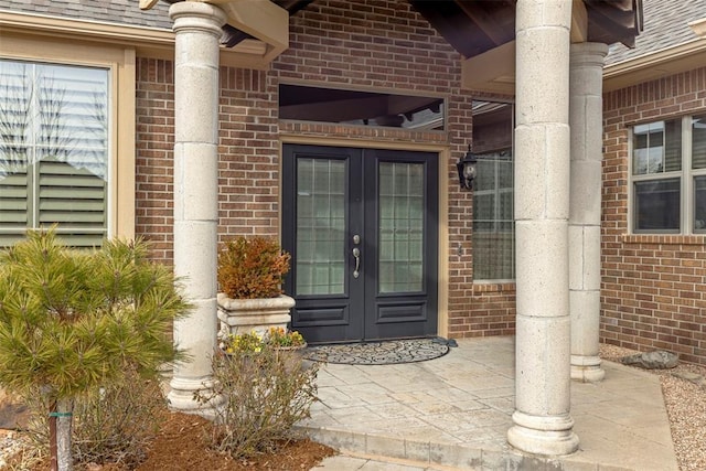 doorway to property featuring brick siding, roof with shingles, and french doors