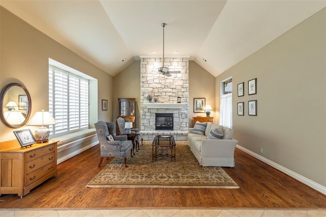 living area featuring baseboards, lofted ceiling, ceiling fan, wood finished floors, and a stone fireplace